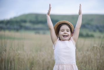 Adorable happy little girl with arms raised up playing in the wheat field on a warm summer day