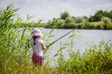 Lonely little fisher girl sitting near a river with a fishing line. Little child fishing