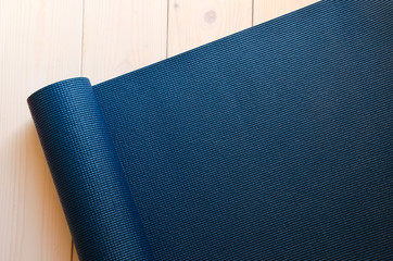 Dark blue mat for yoga, pilates or fitness on wood background. Space for text.