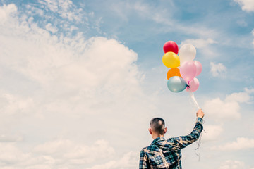 back of Happy young hipster man holding colorful balloons in gra