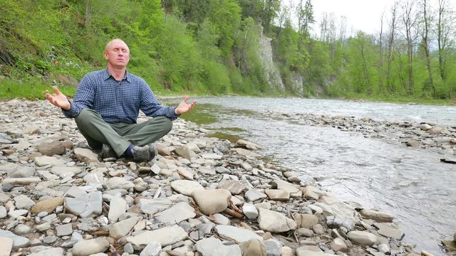 Adult man do meditation near small river. Episode three