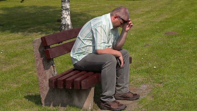 Depressed man crying in the park on bench
