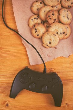 Gamepad and homemade chocolate chip cookies on rustic wooden tab