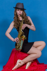 Obraz na płótnie Canvas girl in Pointe and saxophone on a red silk on a blue background in the Studio