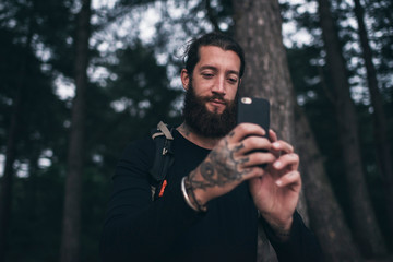 Man with beard in forest taking pictures with smartphone