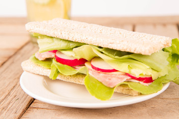 Crispbread sandwich with headcheese, cheese, radish and lettuce and a glass of lemonade