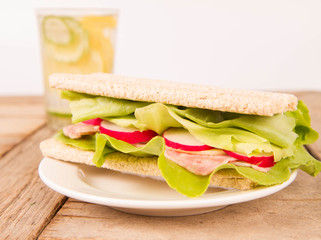 Crispbread sandwich with headcheese, cheese, radish and lettuce and a glass of lemonade