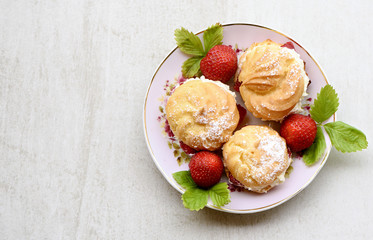 Cream puffs or profiterole filled with whipped cream served with strawberries on a stone grey board for text