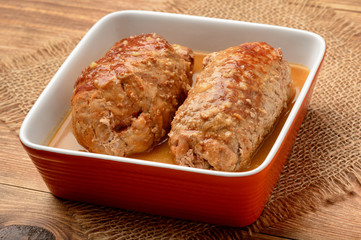 Roasted meat roulades with sauce on wooden background.