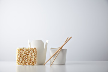 Opened and closed takeaway boxes, brick of fast food noodles presented with chopsticks, isolated on white Retail set
