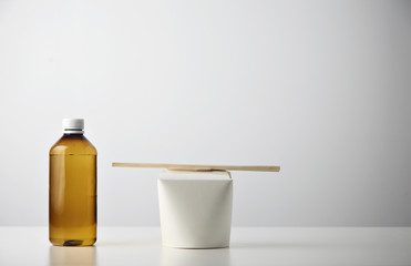 Retail takeaway presentation business set: plastic brown bottle with water on left side of closed blank noodles box with wok noodles inside and chopsticks on top isolated on white