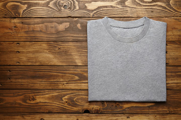 Blank grey t-shirt accurately folded on rustic wooden table top view mockup