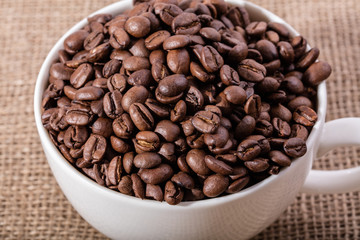 White cup with coffee seeds on jute bag