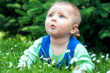 Cute smiling little baby lying on a fresh green grass in a park.