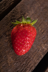 One juicy strawberry on wooden plank