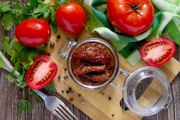 Sun-dried tomatoes in a jar on a wooden table, top view.