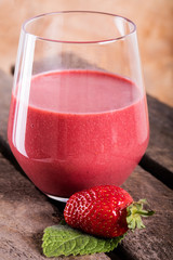 Glass with strawberry cocktail on wooden plank