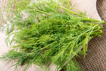 Fresh green dill on wooden cutting board on jute bag