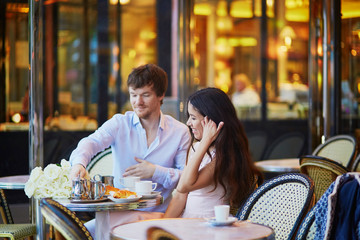 Couple drinking coffee and eating croissants in Parisian cafe