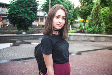 A young girl with beautiful hair and dress a black shirt waiting for friends. She straightens hair at school. The girl walk in a city. Pretty Girl. Wind develops hair