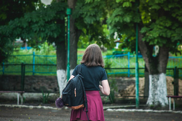 Lonely girl in a black shirt and red skirt with a backpack walking in the park. Girl in a strange place.