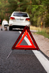 Red warning triangle and broken car in the middle of forrest