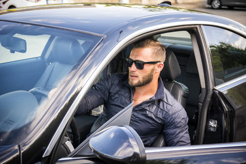 Handsome bearded man going out of car in sunglasses