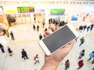 Hand holding smart phone with passengers inside transit station