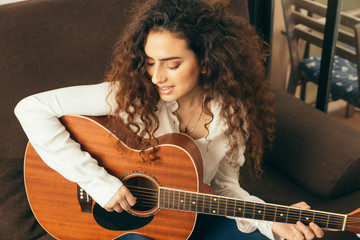 Naklejka premium Girl playing guitar and singing. Young woman with long hair studying music at home. She plays acoustic guitar and sing alone at home.