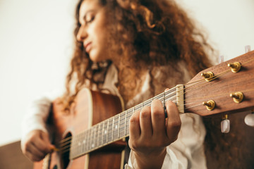 Girl playing guitar and singing. Young woman with long hair studying music at home. She plays...