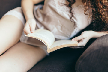 Young girl reading a book on the sofa, with curly hair and fairly dressed