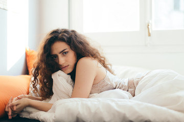 Obraz premium Sexy woman in bed in the morning showing her beautiful body. She doesn't wants to wake up. Awaken with natural light in her bedroom and covered with the bed sheets