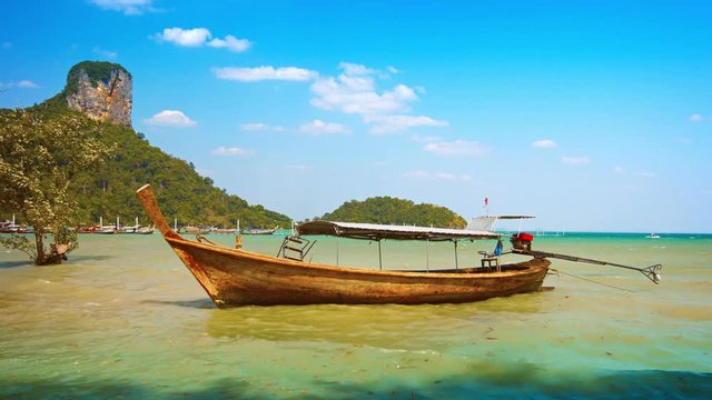 Video 4k - Beautifully handcrafted, wooden longtail boat, anchored near a popular tropical beach at high tide, beneath a towering limestone outcrop.