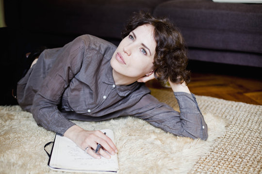 Thoughtful young woman lying on rug while writing music on notepad