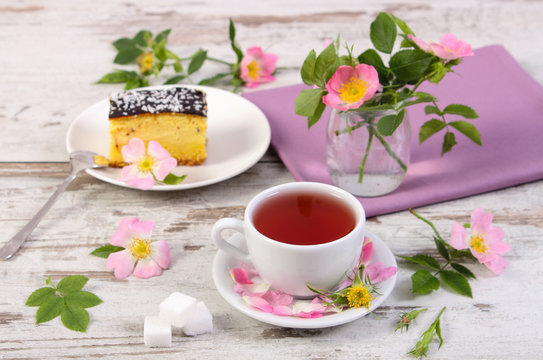 Cup of tea with cheesecake and wild rose flower on old wooden background