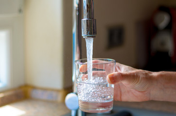 Woman filling a glass of water from a tap - obrazy, fototapety, plakaty