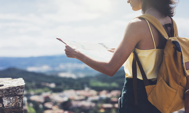 Hipster young girl with bright backpack looking at a map and poining hand the travel plan. View from the back of the tourist traveler on background mountain, sea, binoculars. Mock up for text message