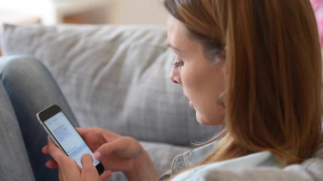 Woman using smartphone relaxed on sofa