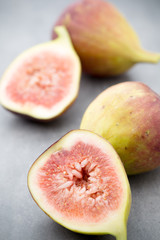 Whole figs and one fig sliced in half on top of a gray table.