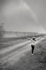 Fototapeta na wymiar The girl happily waved his hands to the sky, standing with your back near a country road, a black and white image.