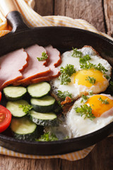 Homemade breakfast: fried eggs with ham and vegetables in a pan close-up. vertical
