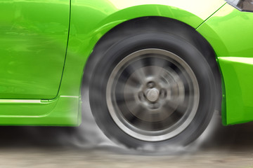 Green car racing spinning wheel burns rubber on floor.