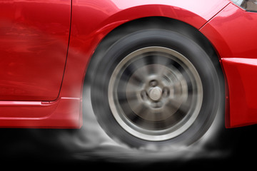 Red car racing spinning wheel burns rubber on floor.