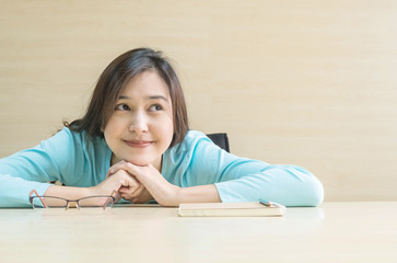 Naklejka premium Closeup asian woman lied on desk with happy face in rest time from reading a book on blurred wooden desk and wall textured background in the meeting room , happy time and relaxation of woman concept