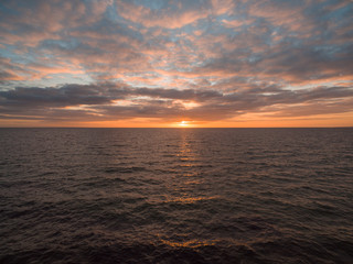 Orange sunset over water with sun peeking out of the clouds
