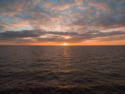 Orange sunset over water with sun peeking out of the clouds