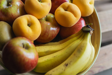 Fruit bowl full of bananas, apple, peaches and kiwi, on a table made of wood with natural light