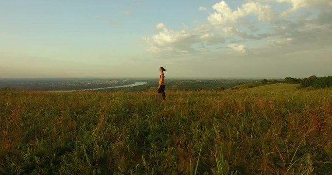 Camera flying around young woman doing yoga in the field. Fruska gora, Novi Sad, Serbia.