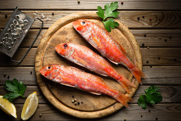 Fresh fish red mullet with lemon and seasonings on an cutting board Top view