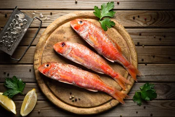 Poster Fresh fish red mullet with lemon and seasonings on an cutting board Top view © greenazya